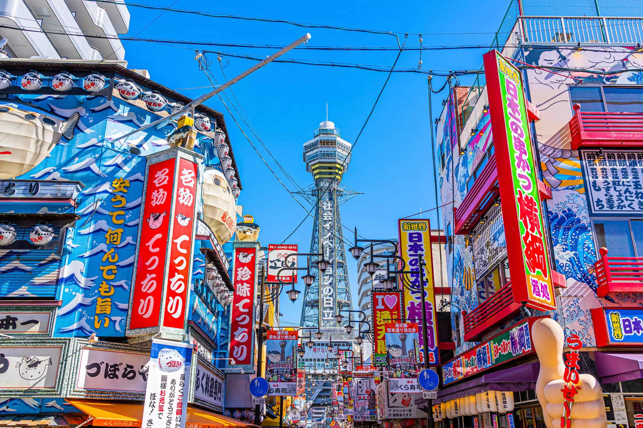 View of the Tsūten-kaku building at the end of street packed with colorful signs and buildings. 