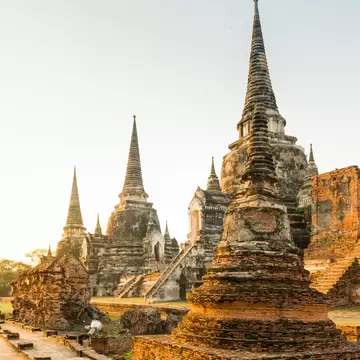 Tall pointed stone stupas and crumbling red-brick ruins beside a brick walkway, lit by warm early-morning sun.