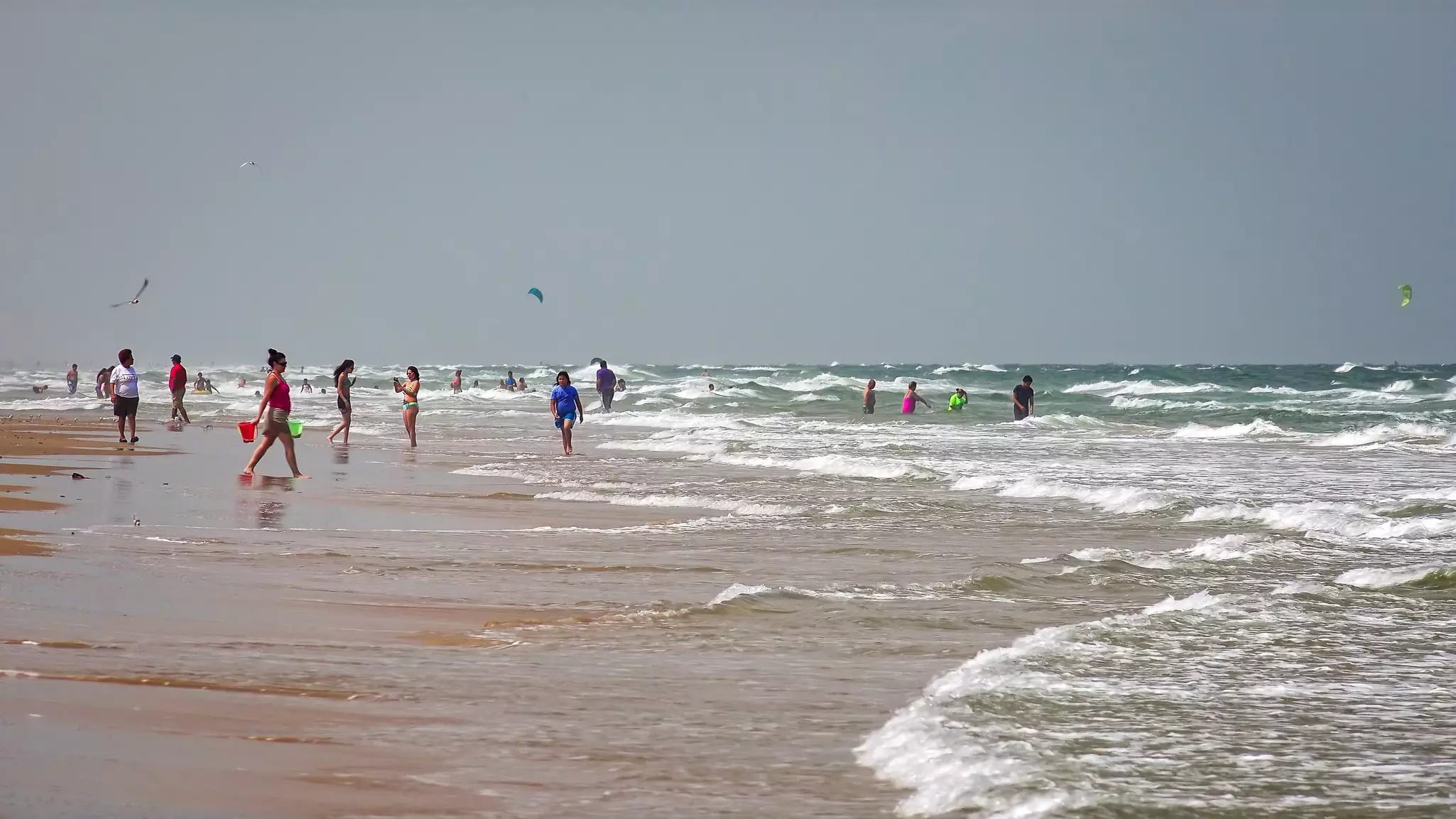 People wade into the white-capped waves that lap a wide beach.