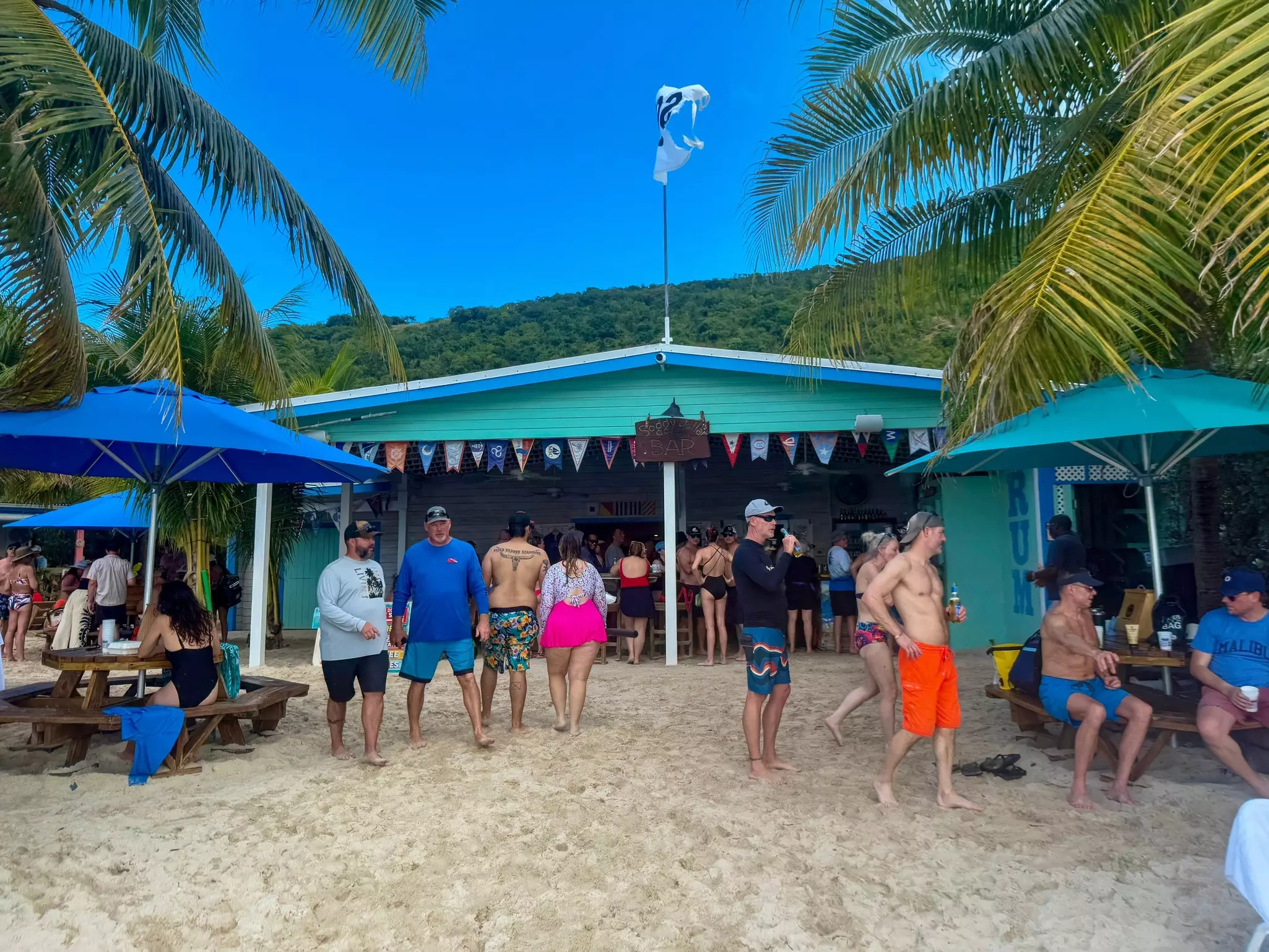 People stand on the sand in front of a beachfront bar.