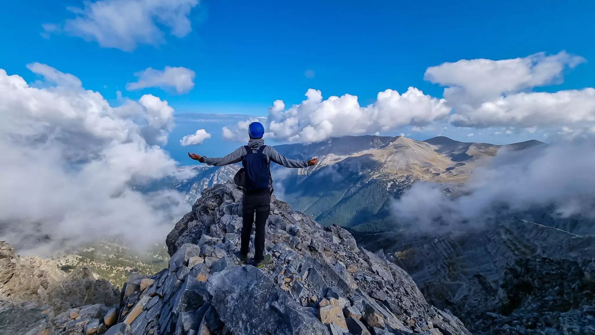 Rear view of man with open arms on cloud-covered mountain summit