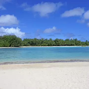 White sand beach facing a turquoise lagoon and a low islet covered in palms and ironwood trees