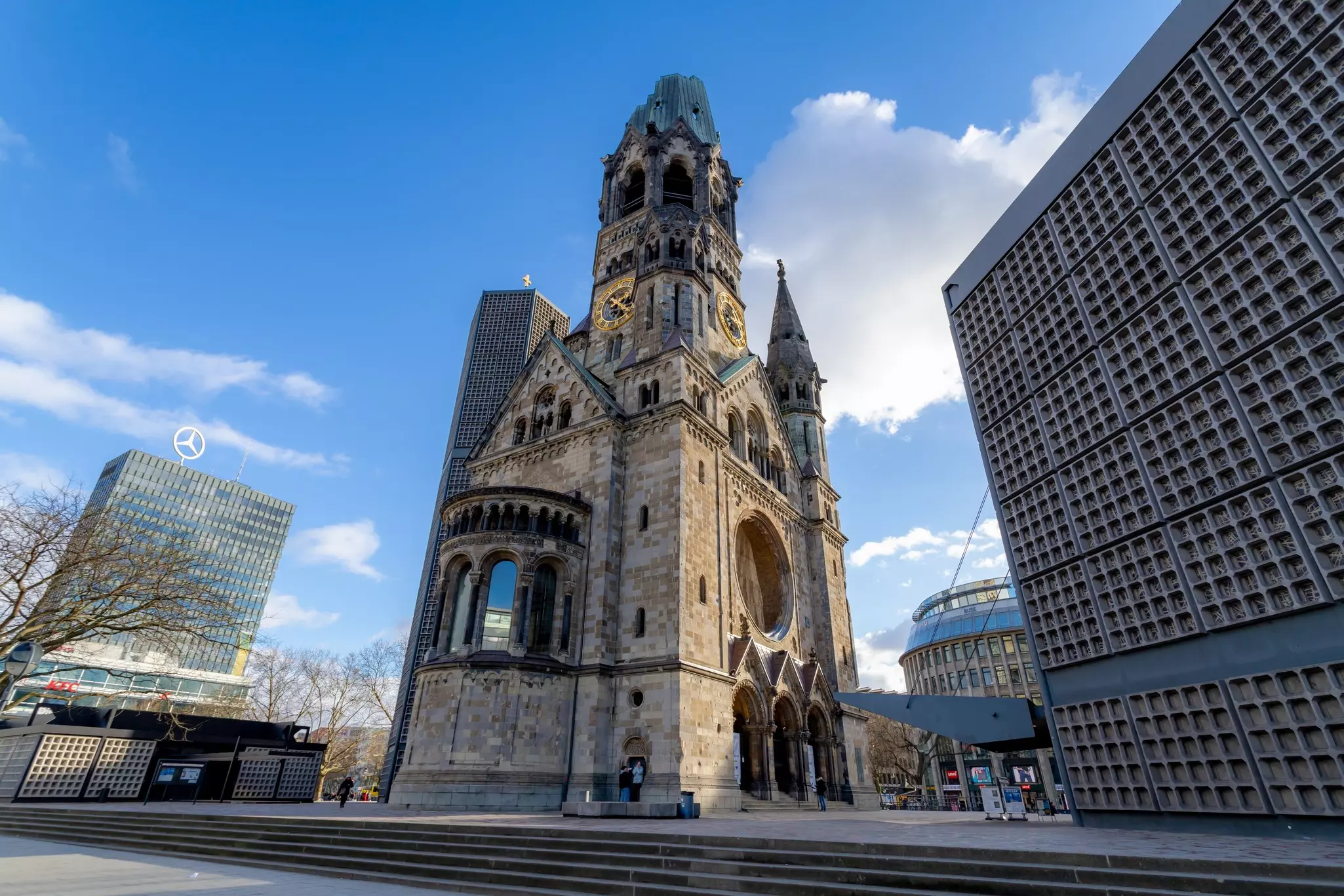 A large stone church with city buildings in the background on a sunny day.