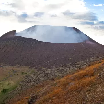 A red dusty landscape on the slopes of a smoking volcano crater.