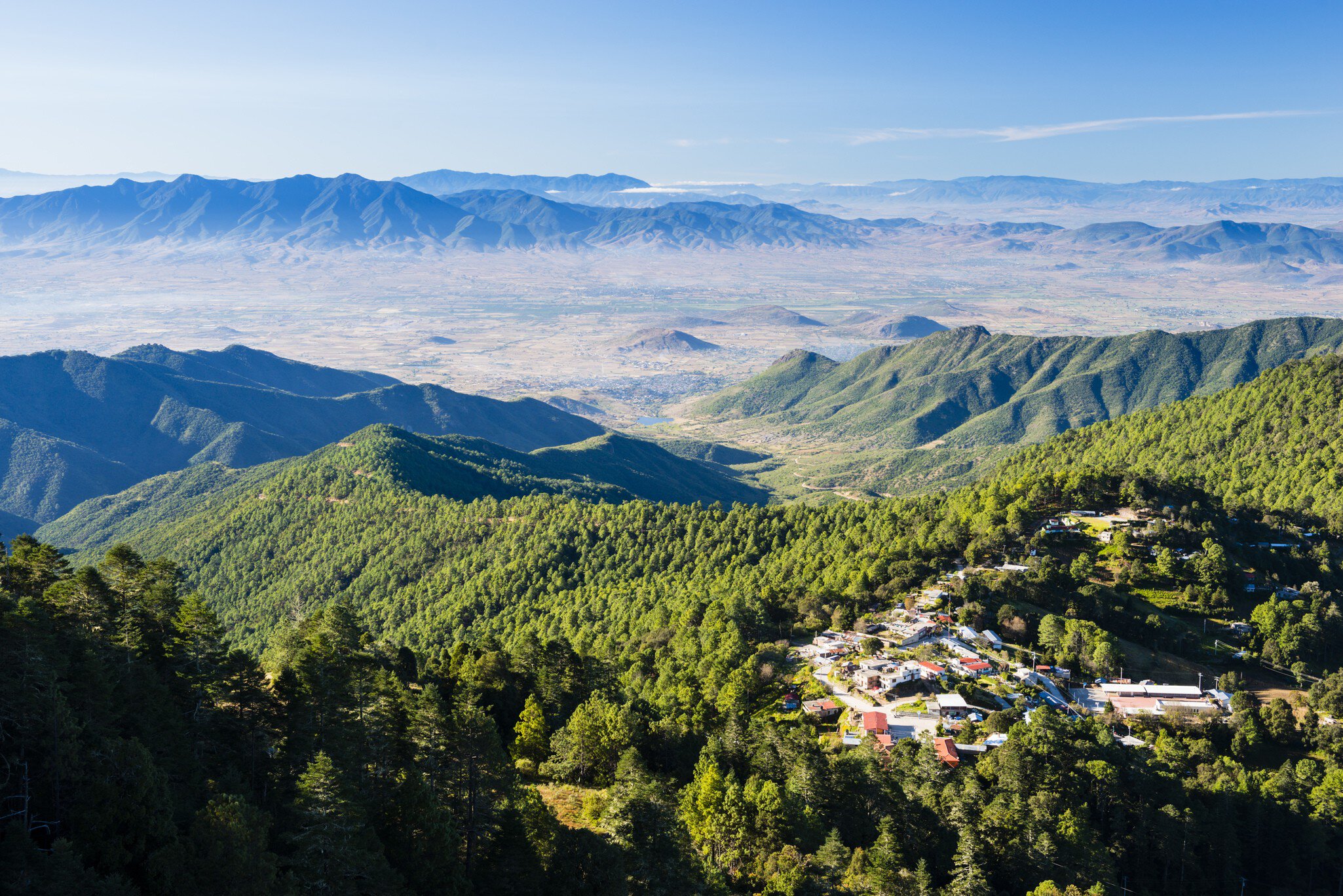 Forested mountains with a small village and a distant hazy valley.