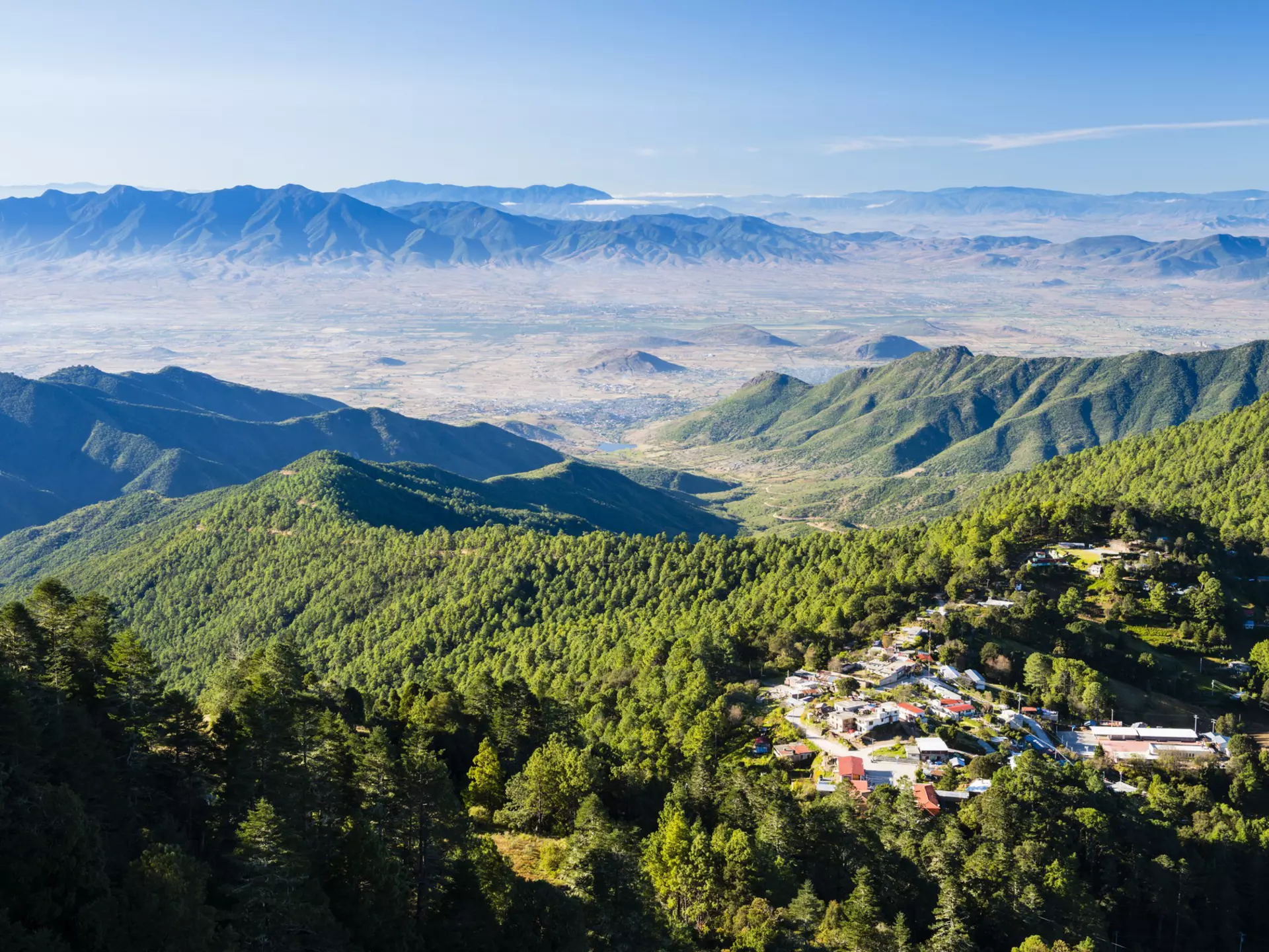 Forested mountains with a small village and a distant hazy valley.