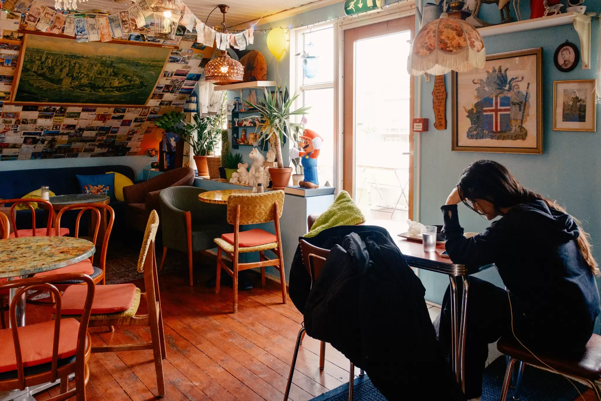 A person alone at a table in a brightly colored cafe with empty tables.