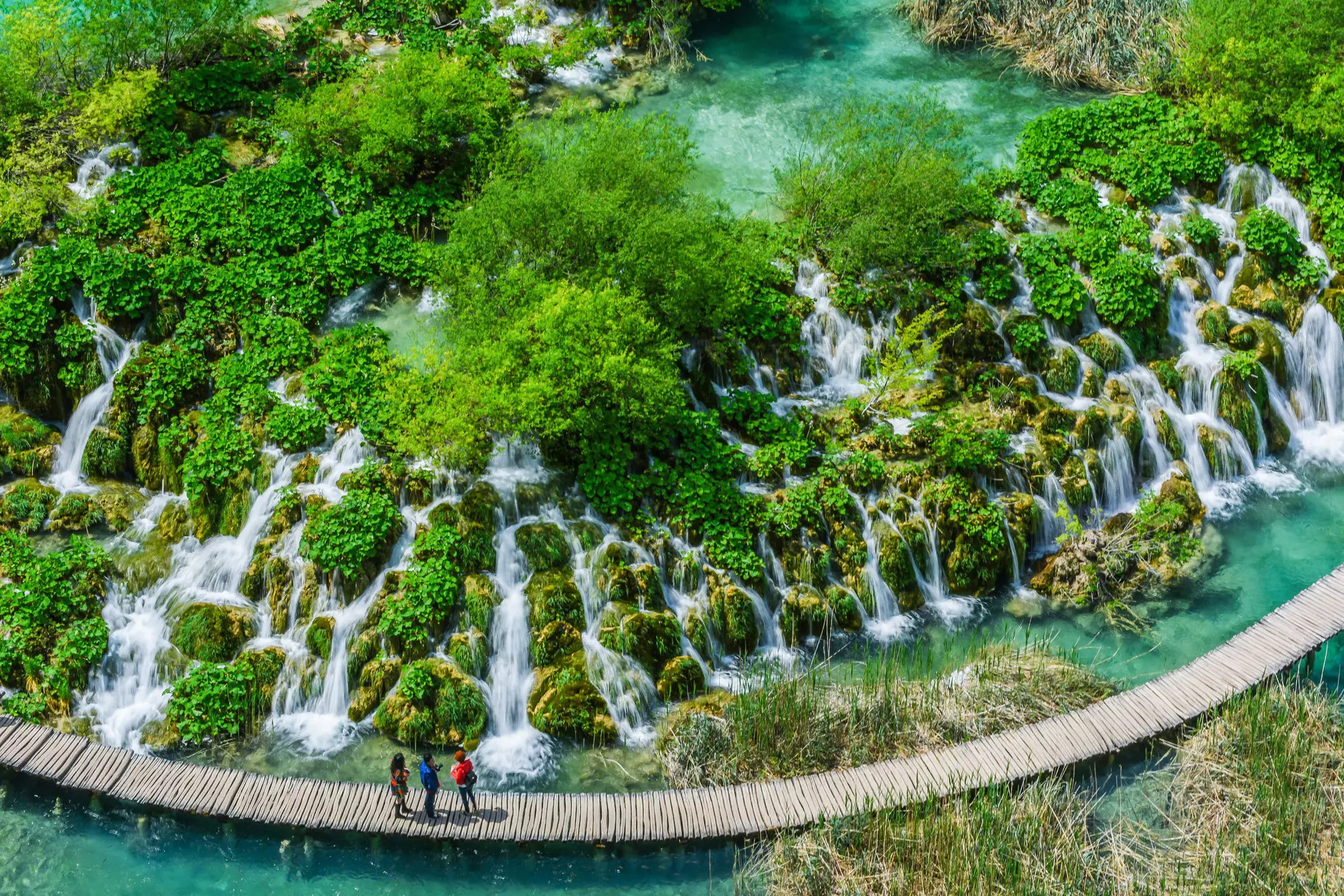 People stand on a boardwalk admiring the waterfalls of Plitvice Lakes National Park.