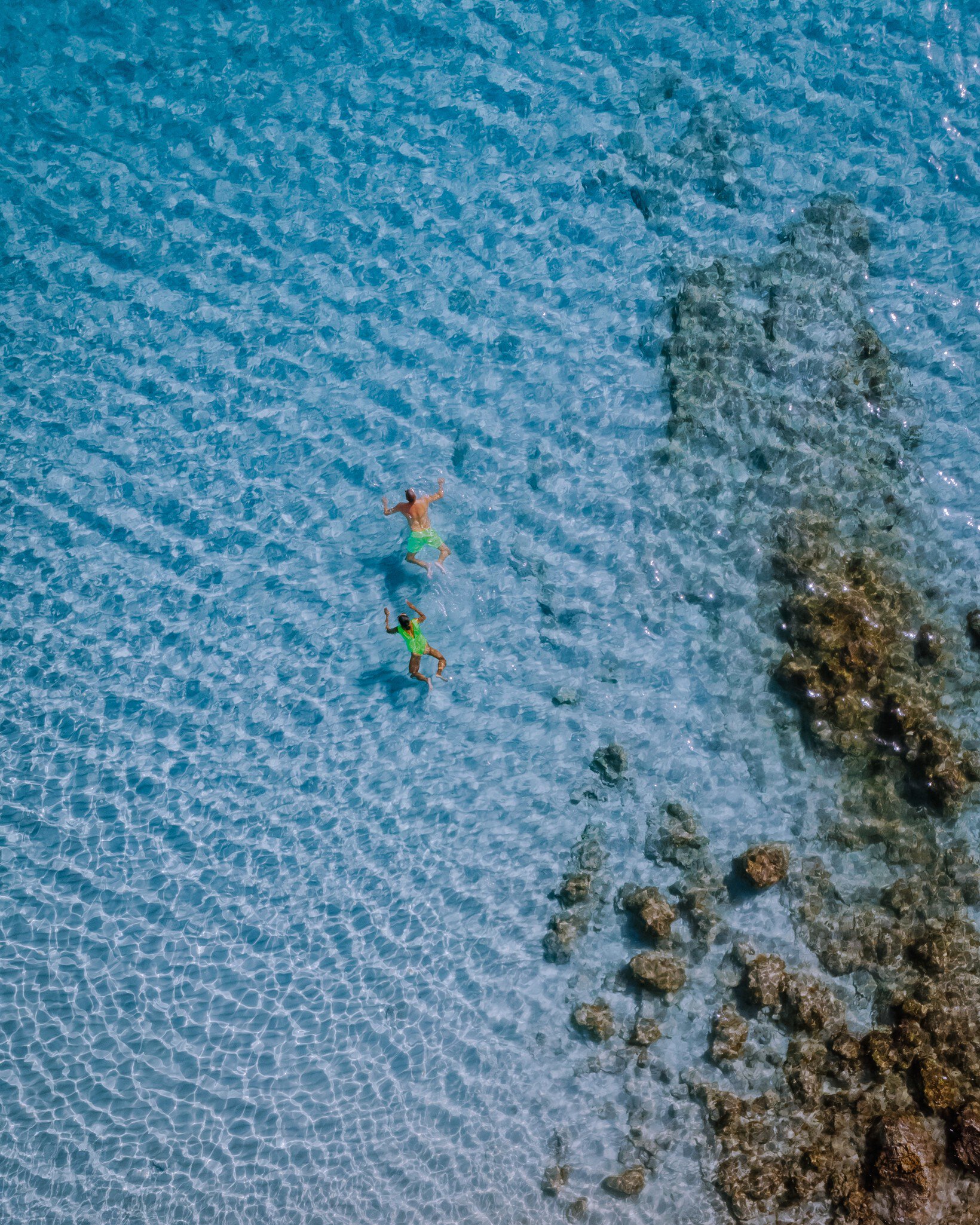 A couple wearing green swimsuits relax and swim in the crystal clear water of Balos beach.