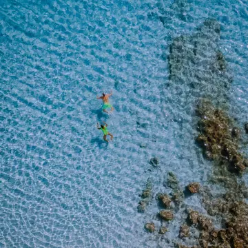 A couple wearing green swimsuits relax and swim in the crystal clear water of Balos beach.