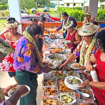 Cook Islanders line up at each side of a long table laden with different dishes during a traditional island celebration