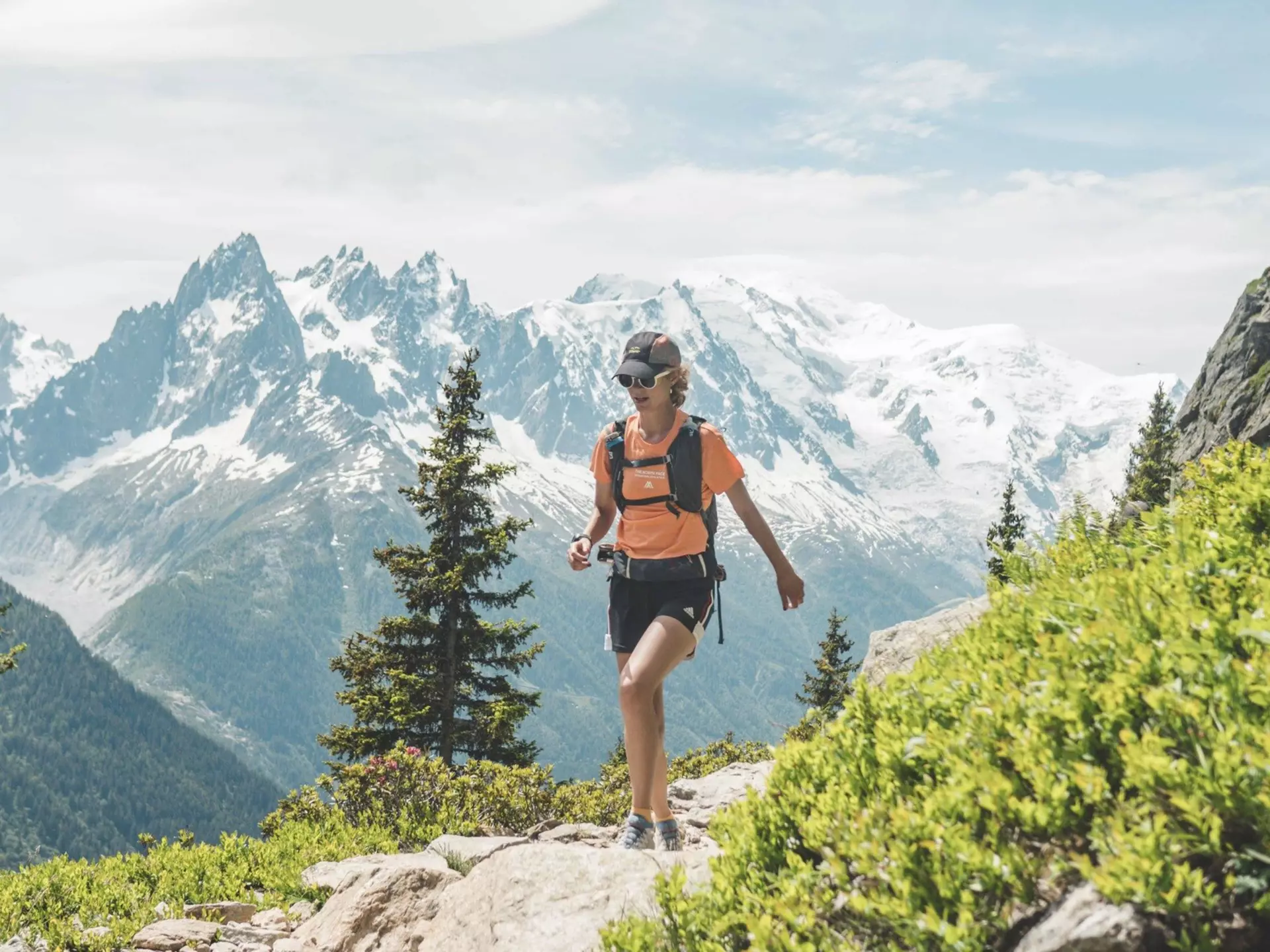 Hiker walking along a mountain path on the Tour du Mont Blanc with snowy peaks in the background. Quentin Boehm