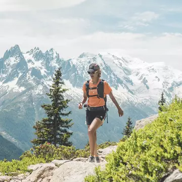 Hiker walking along a mountain path on the Tour du Mont Blanc with snowy peaks in the background. Quentin Boehm