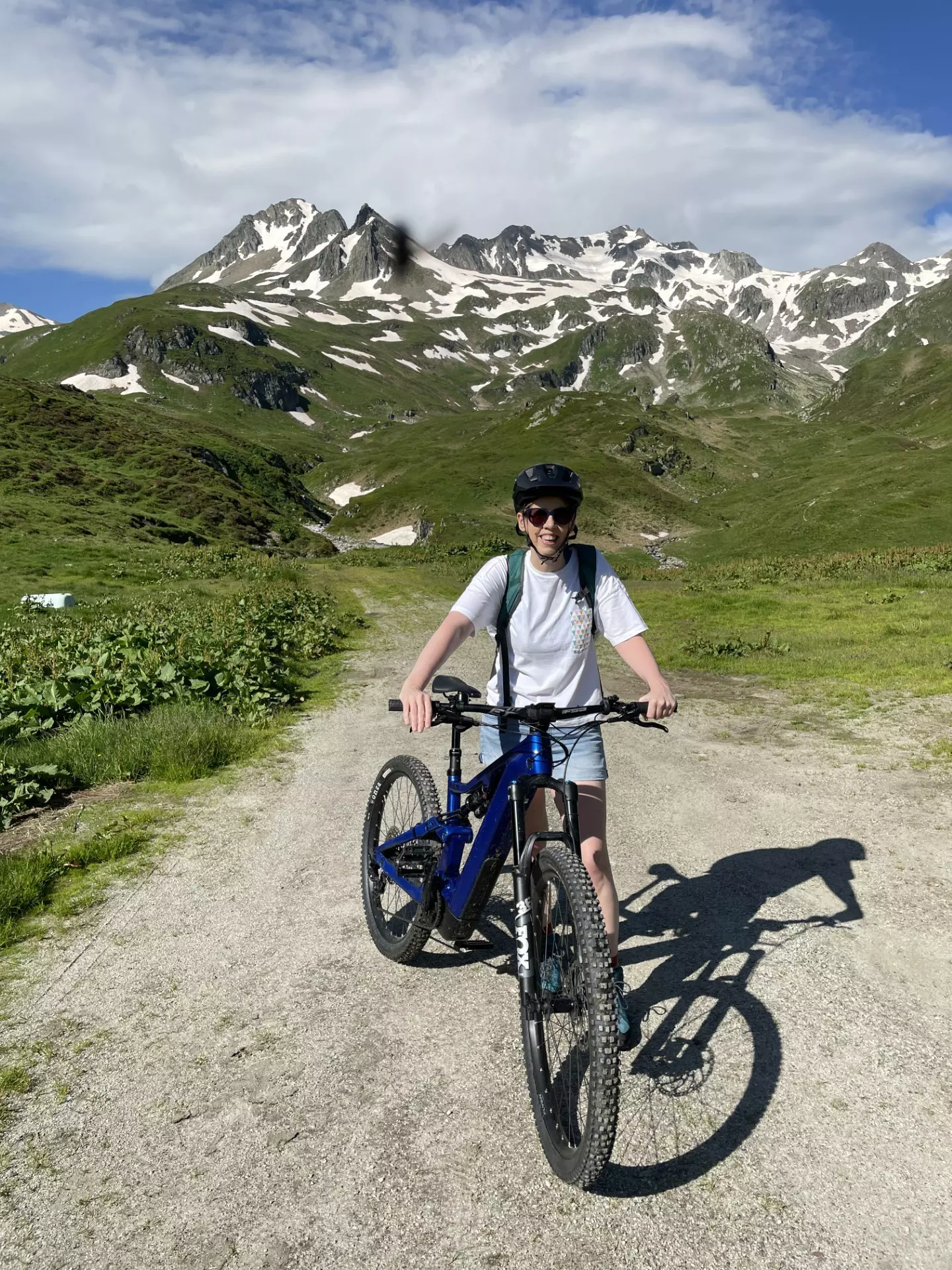 A woman stands next to a bike in an alpine meadow