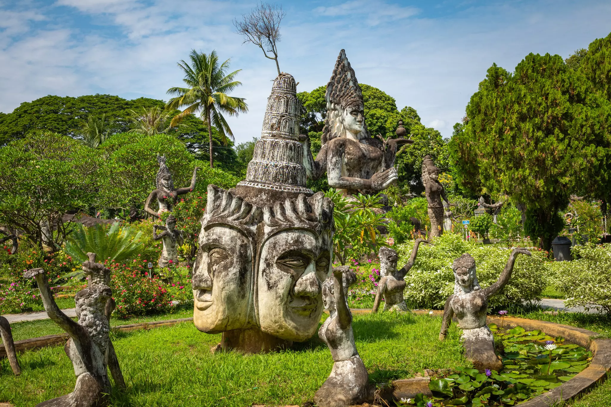 A view of sculptures of Buddhas and other deities in a tropical garden.