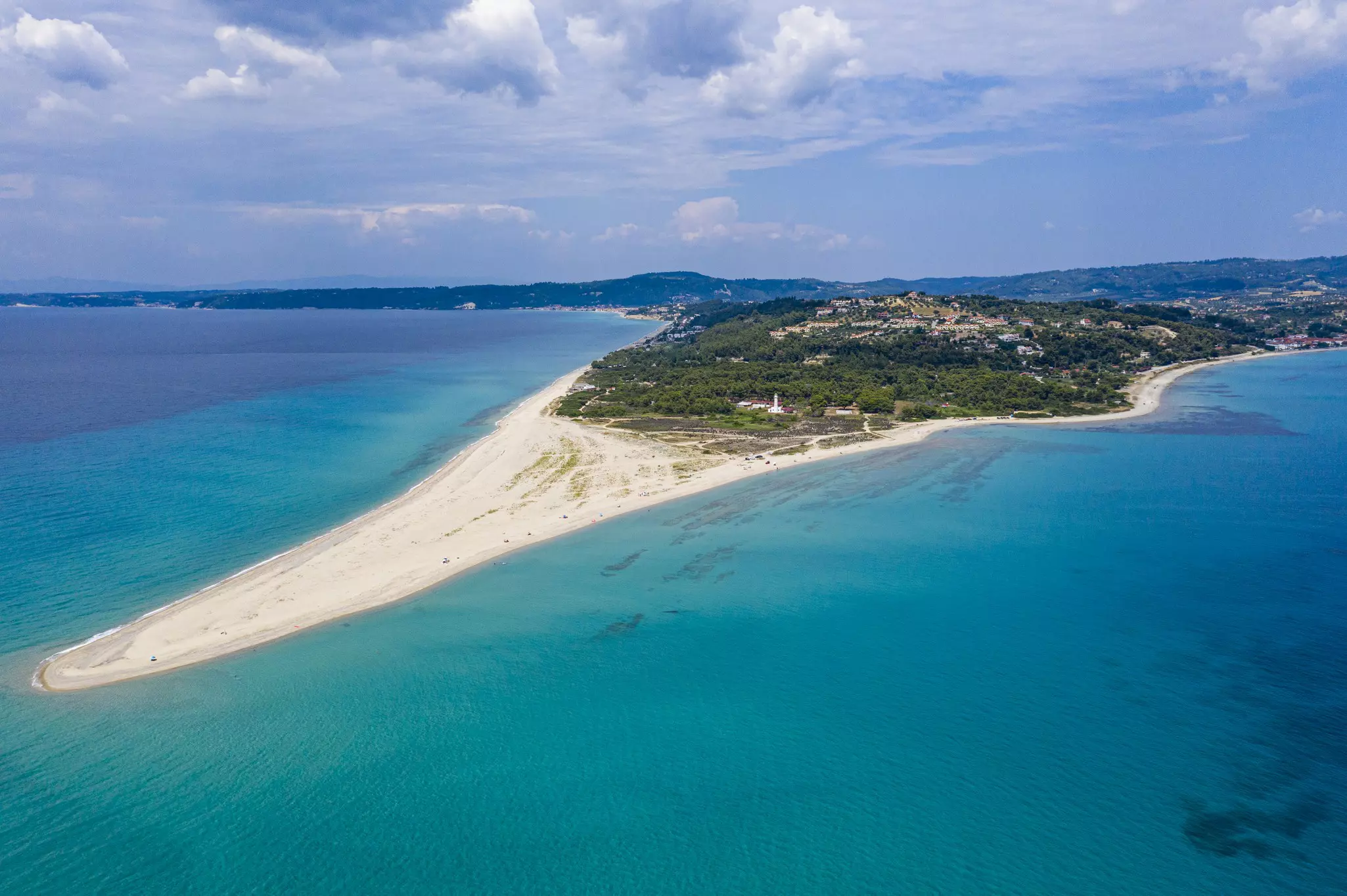 An aerial view of a triangular shaped beach protruding from a forested island.
