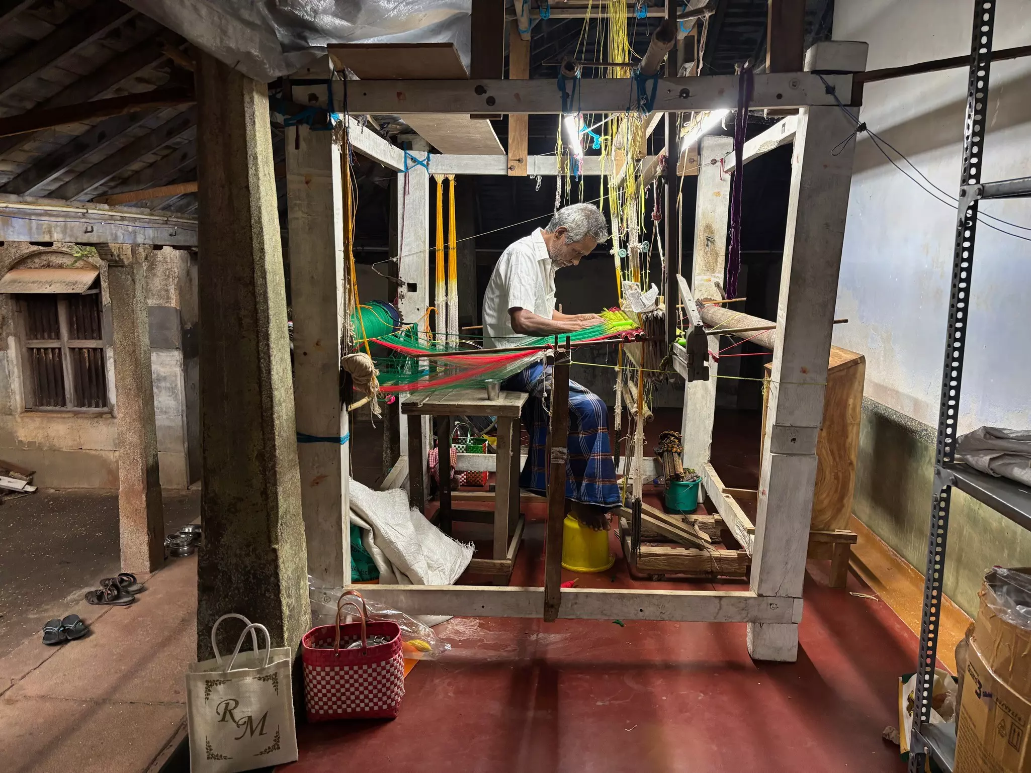 A weaver leans over a loom as he sews textiles by hand.