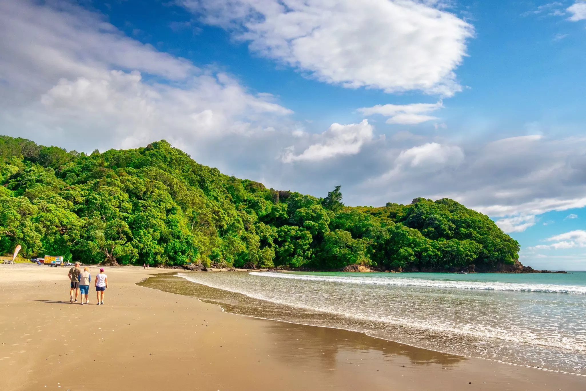 People walk on a golden sandy beach toward lush vegetation at the other end of the cove.