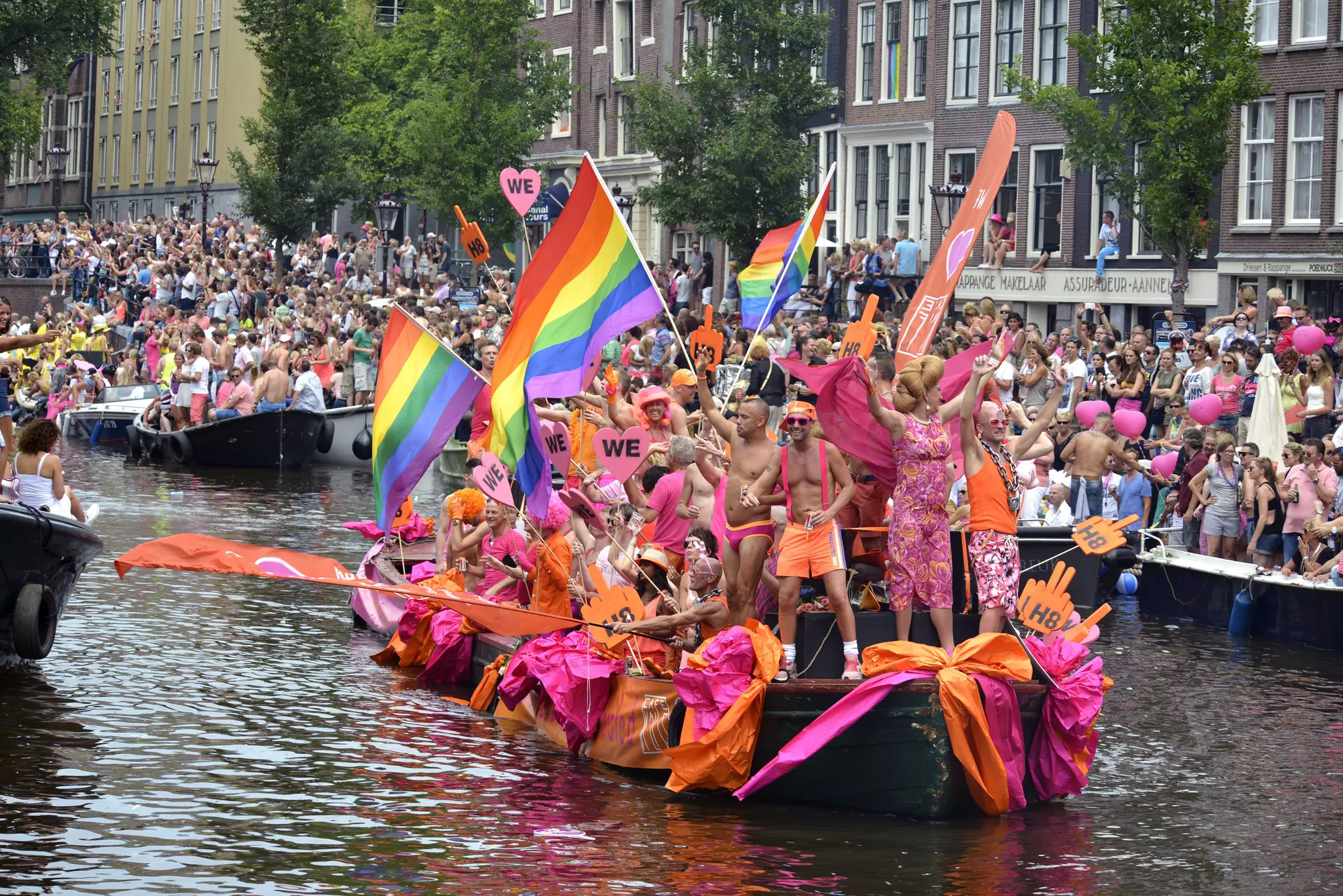 A group of people in pink carrying rainbow flags on the river in Amsterdam.