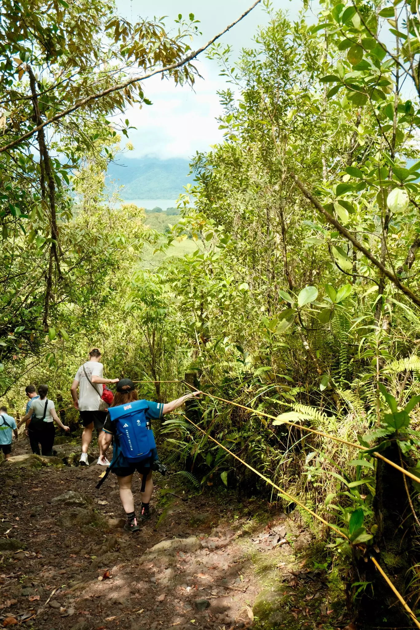 A group of hikers trek down a rocky path, holding onto a rope for stability