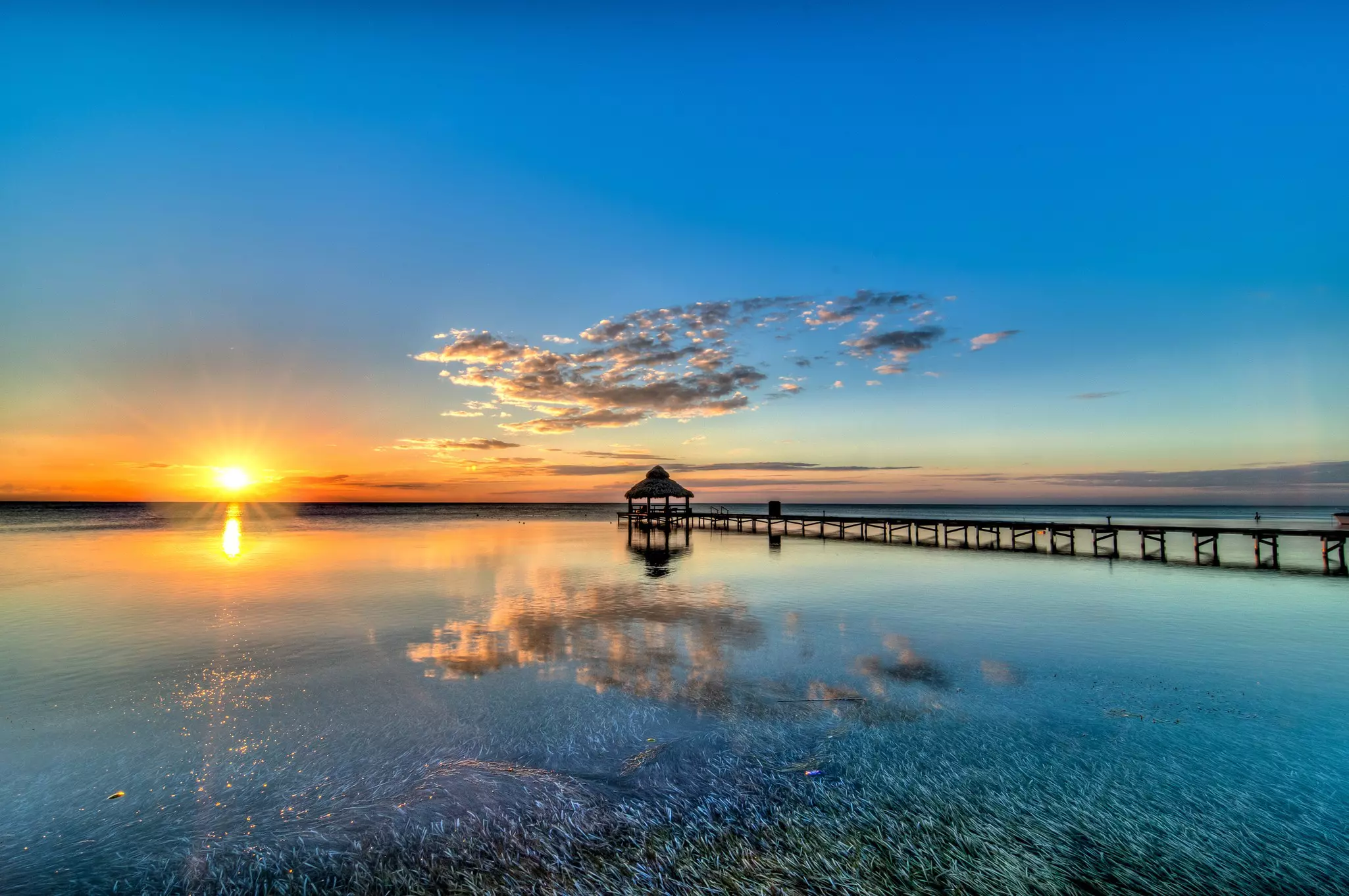 An orange sunset streaks the sky over the ocean with a pier appearing as a silhouette