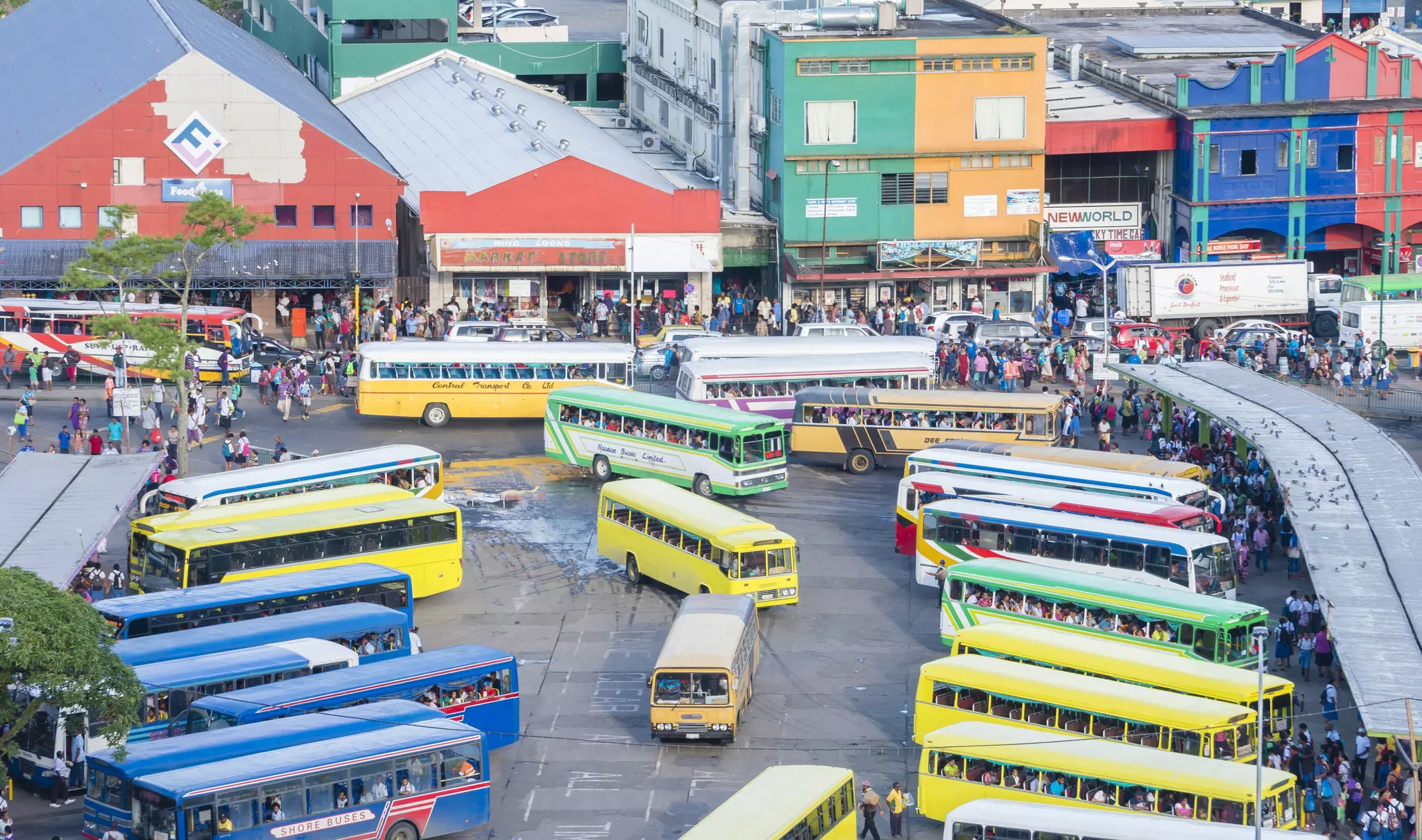 A busy bus terminal, with many brightly colored buses picking up passengers.