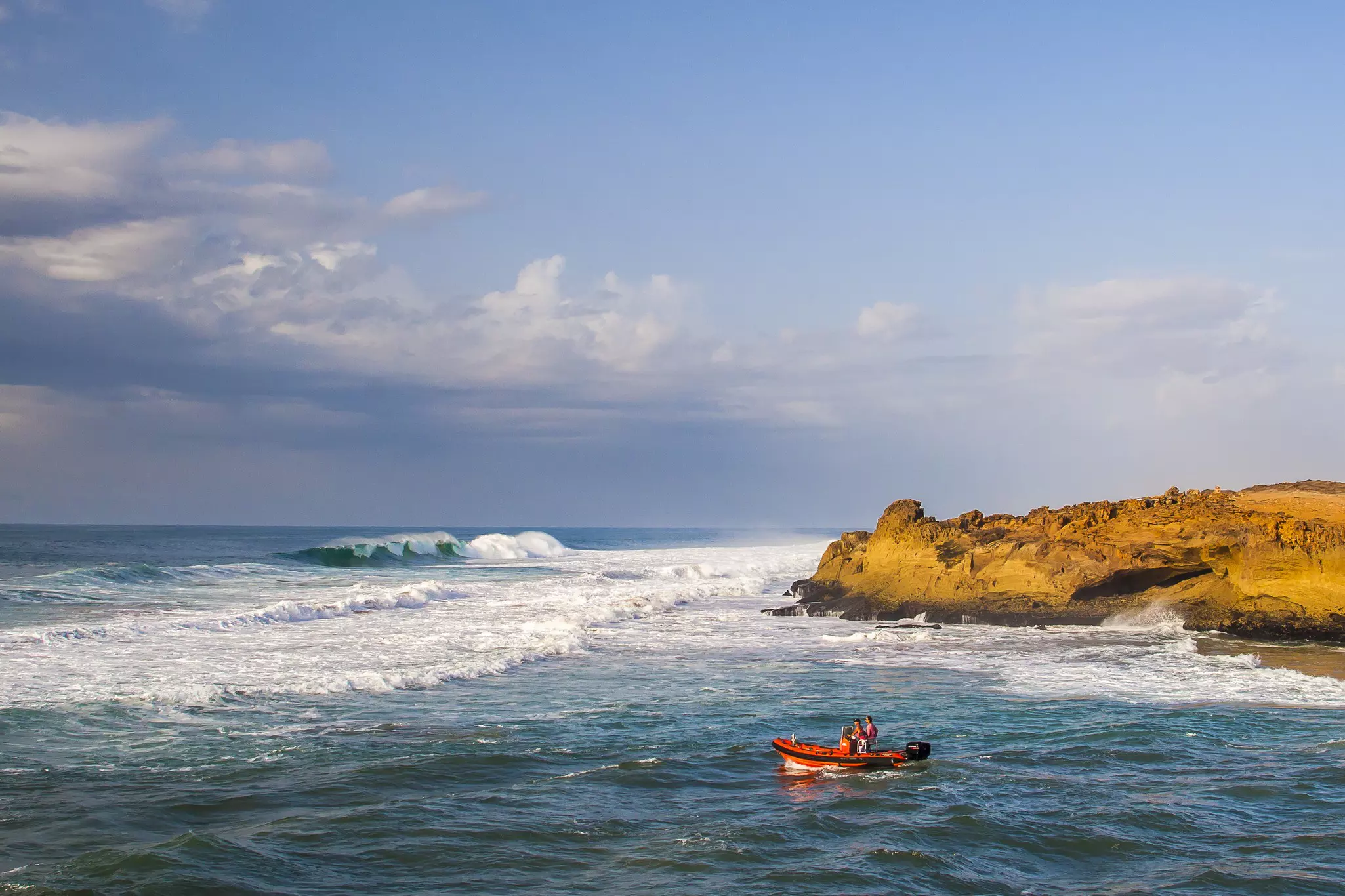 Two men in a red motorboat head out to the surf at Oualidia beach