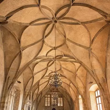 A room with a high, earth-toned ceiling with patterns. Large chandeliers hang in the middle of the room, which has large windows.