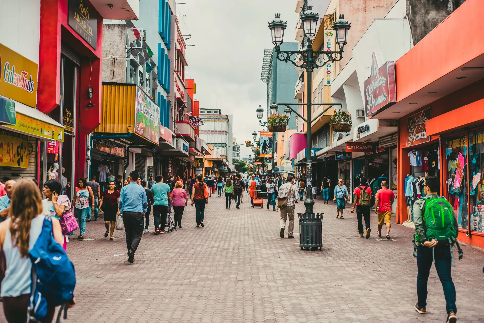 Busy pedestrian street in San José, Costa Rica, lined with colourful shopfronts, ornate lampposts and hanging planters