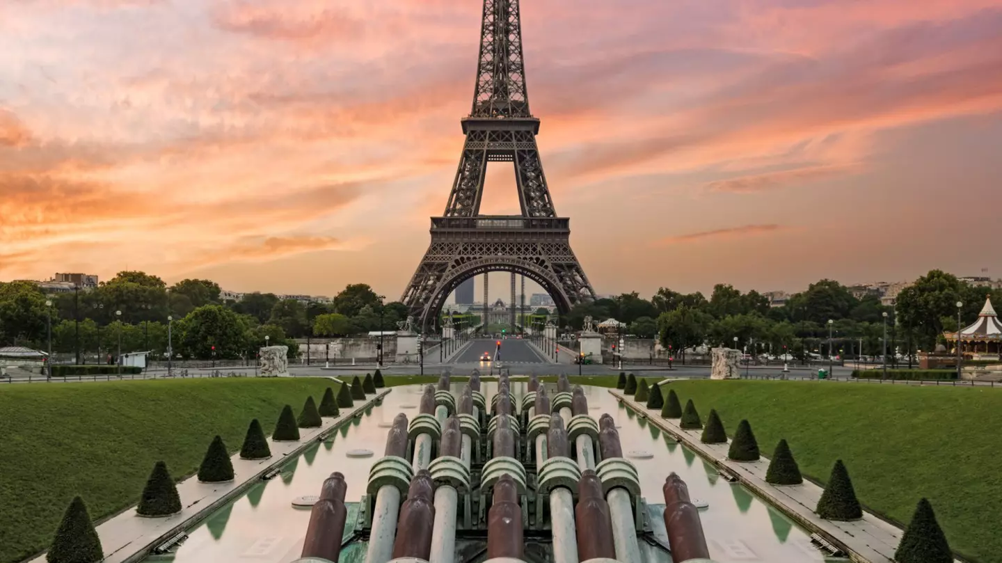 The Eiffel Tower at sunrise. The sky is blue and pink behind the structure.
