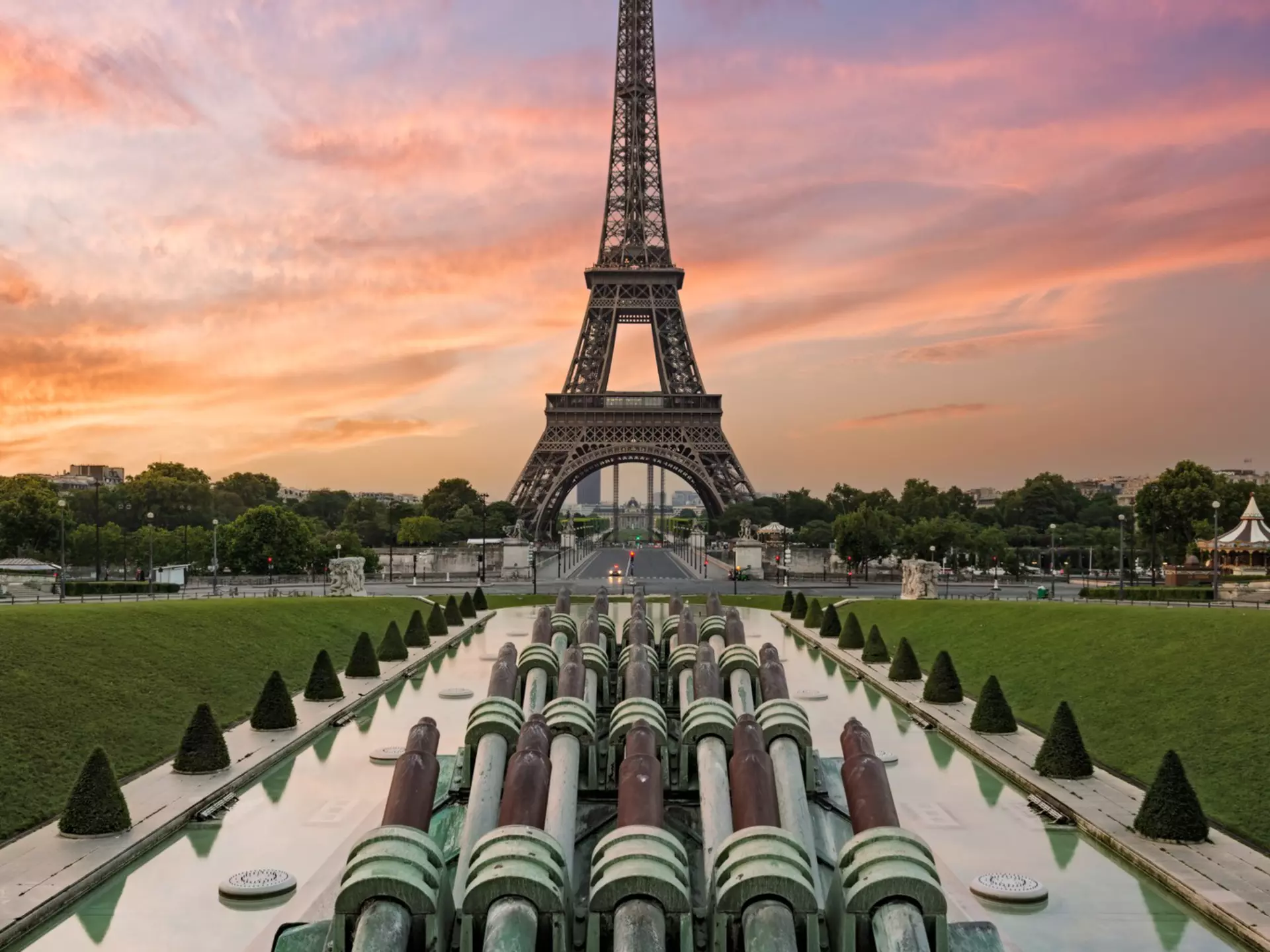 The Eiffel Tower at sunrise. The sky is blue and pink behind the structure.