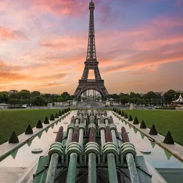 The Eiffel Tower at sunrise. The sky is blue and pink behind the structure.