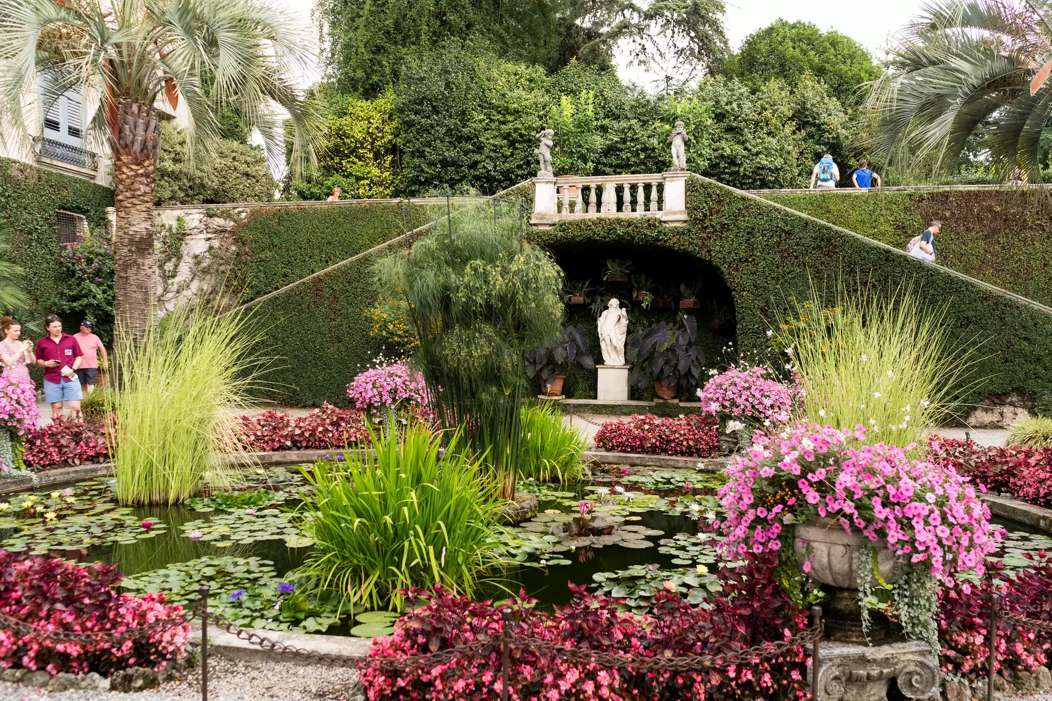 Visitors explore the lush green gardens surrounded by palm trees at the Palazzo Isola Madre.