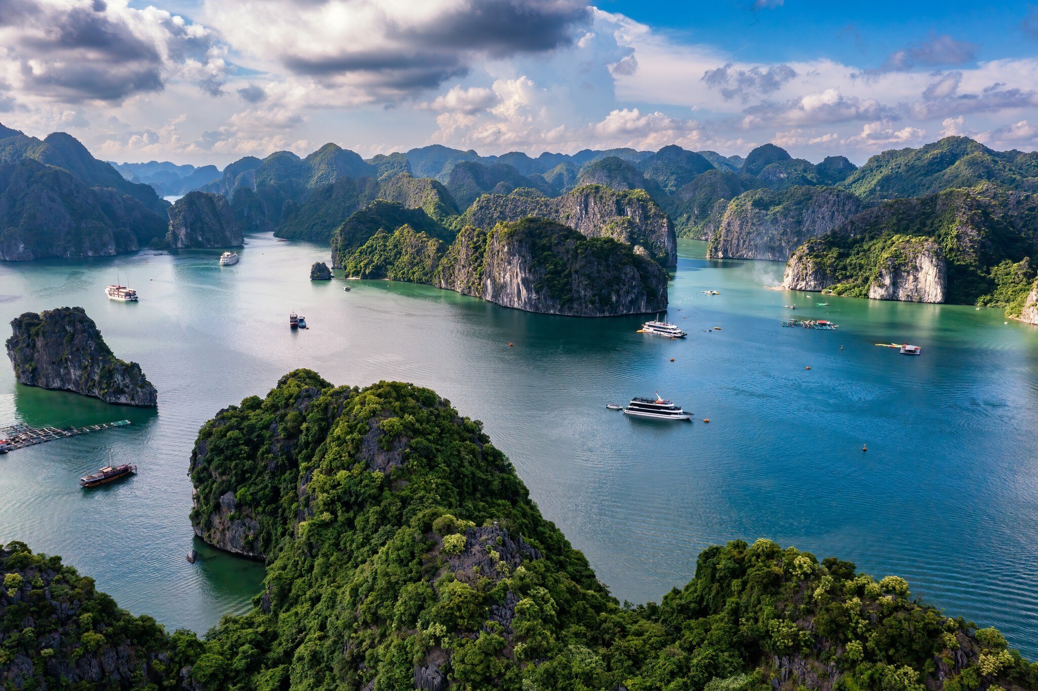 Forested limestone islands and moored boats in the green water of Lan Ha Bay