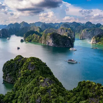 Forested limestone islands and moored boats in the green water of Lan Ha Bay