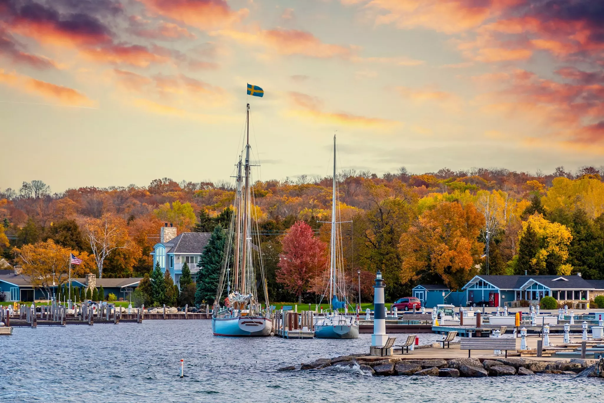 A small harbor town with sail boats moored in the dock. Trees are all golden, marking autumn months.