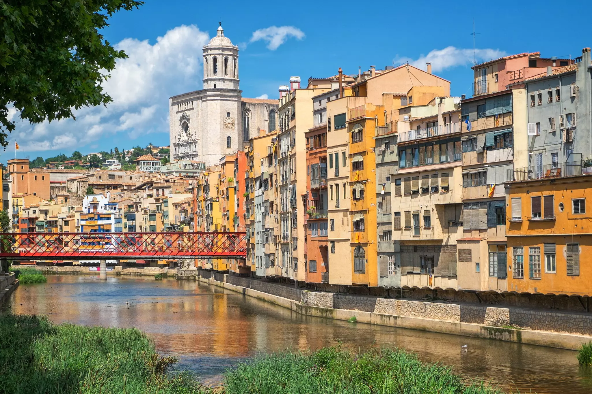 A bright red iron bridge stands out against the colorful buildings overlooking a river.
