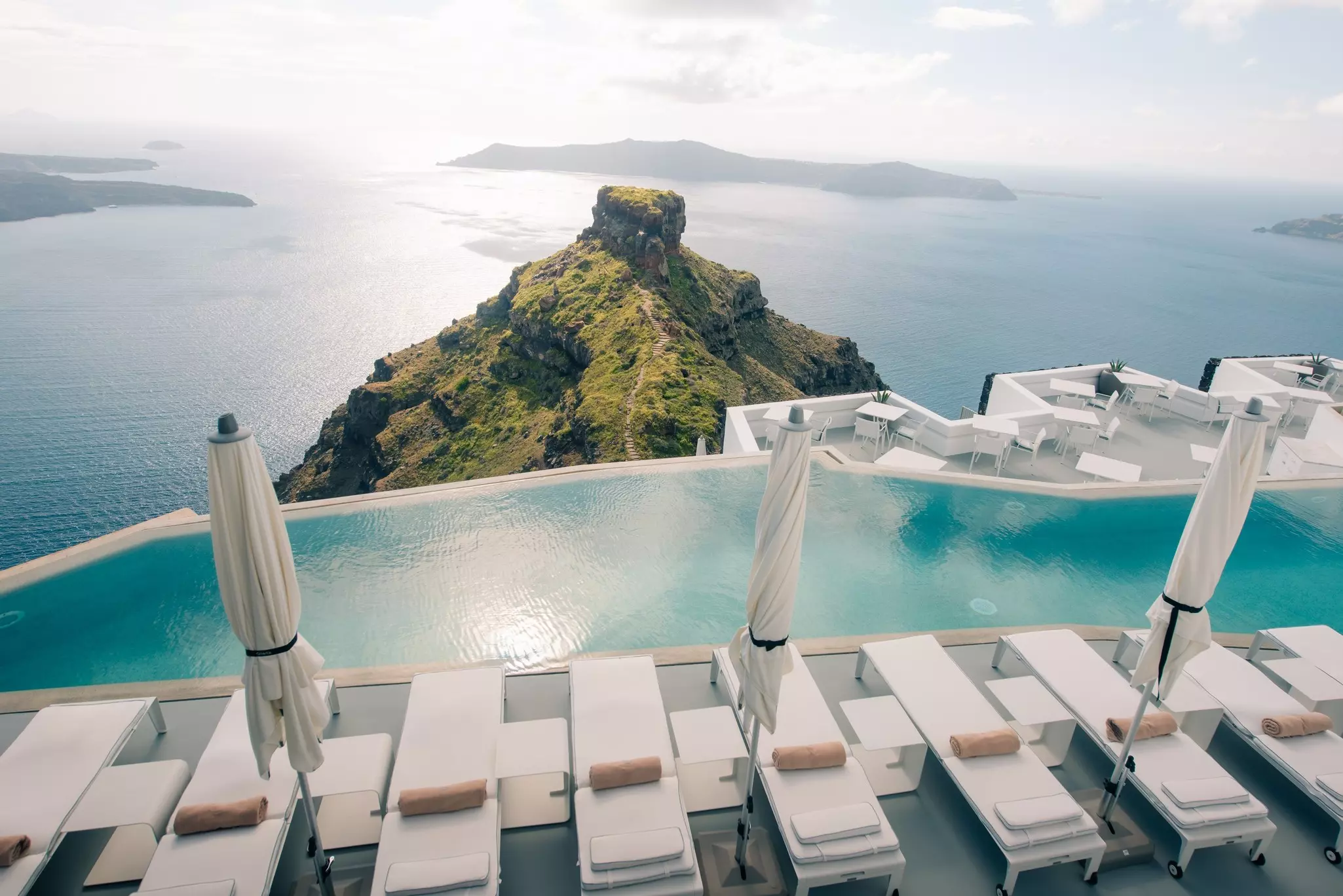 Sun loungers by a pool on a hillside above the sea.