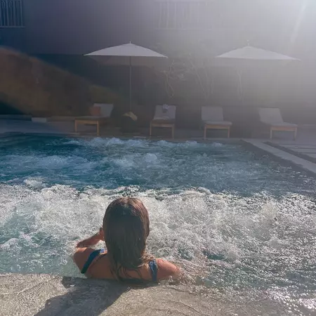 A person wearing sunglasses and a green T-shirt sits outside holding a bottle of Tecate beer. 