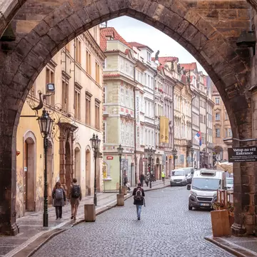 A person walks through a historic city center with cobblestone streets on the other side of an archway.