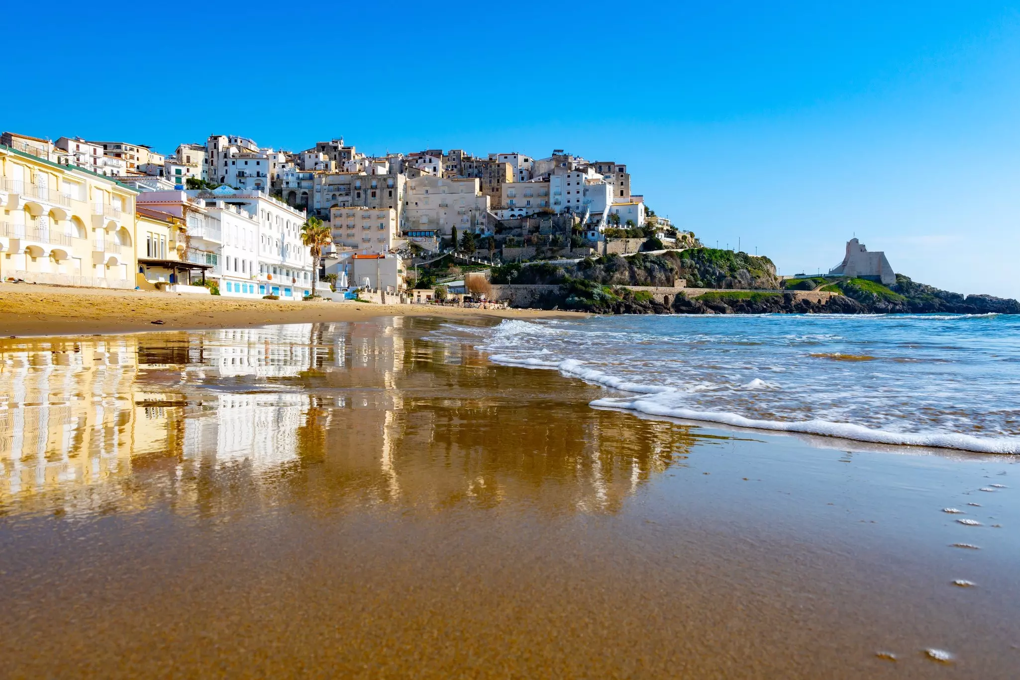 A sandy beach at the edge of a town, lapped by gentle waves.