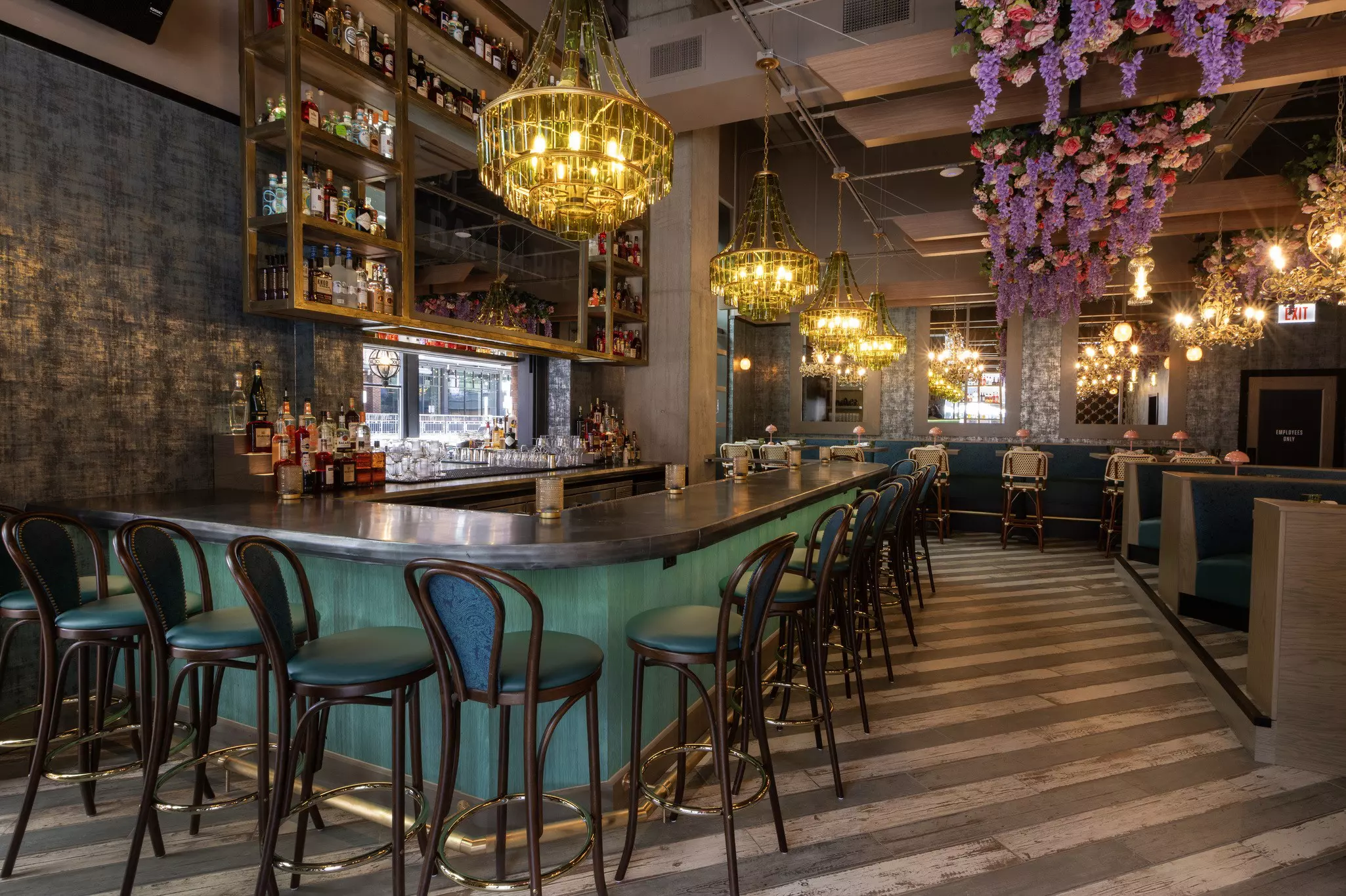 Stools set around a turquoise-colored bar; there are booths in a matching color and chandeliers hanging from the ceiling.