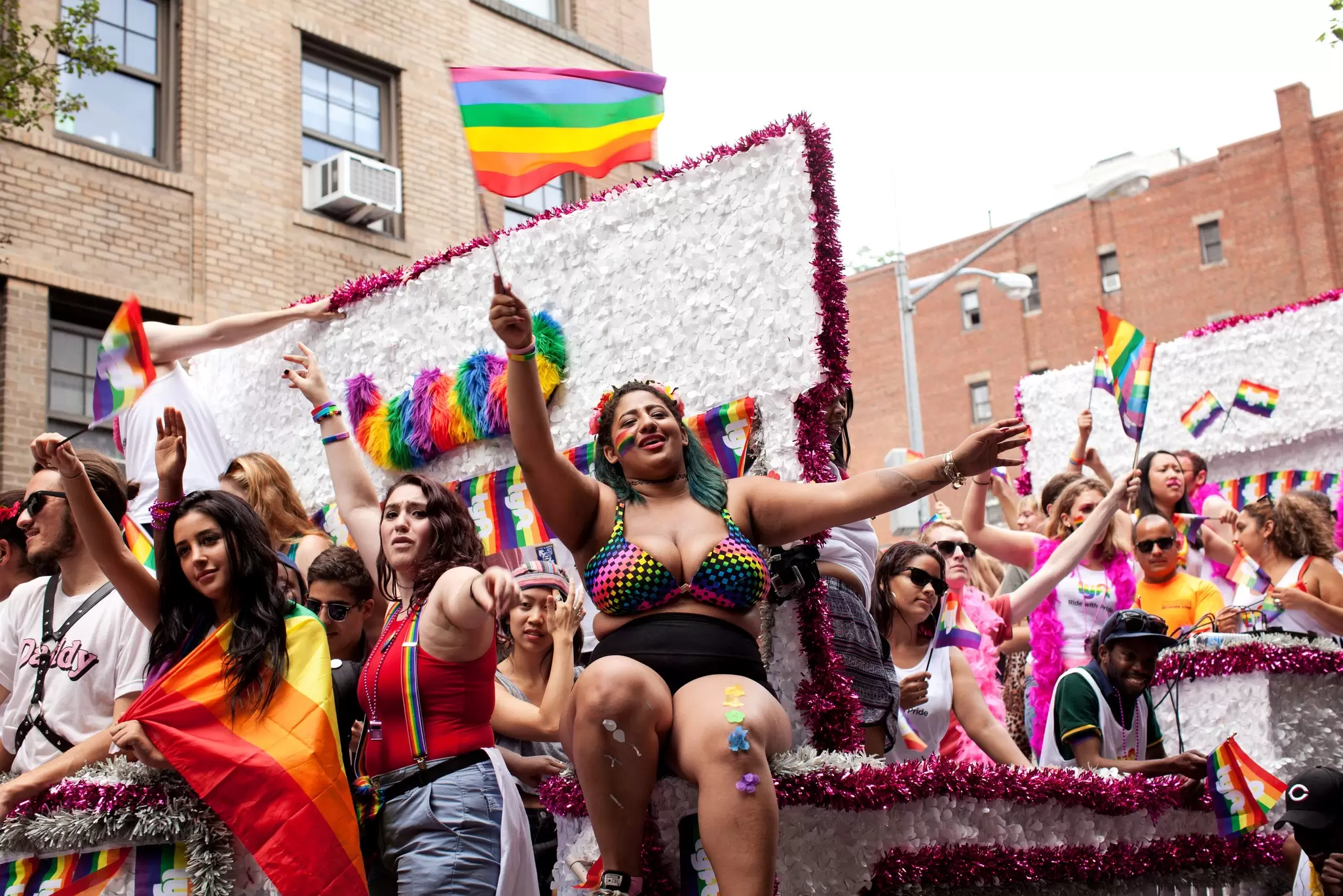People dressed in bright colors and waving Pride flags on a float in the NYC Pride parade