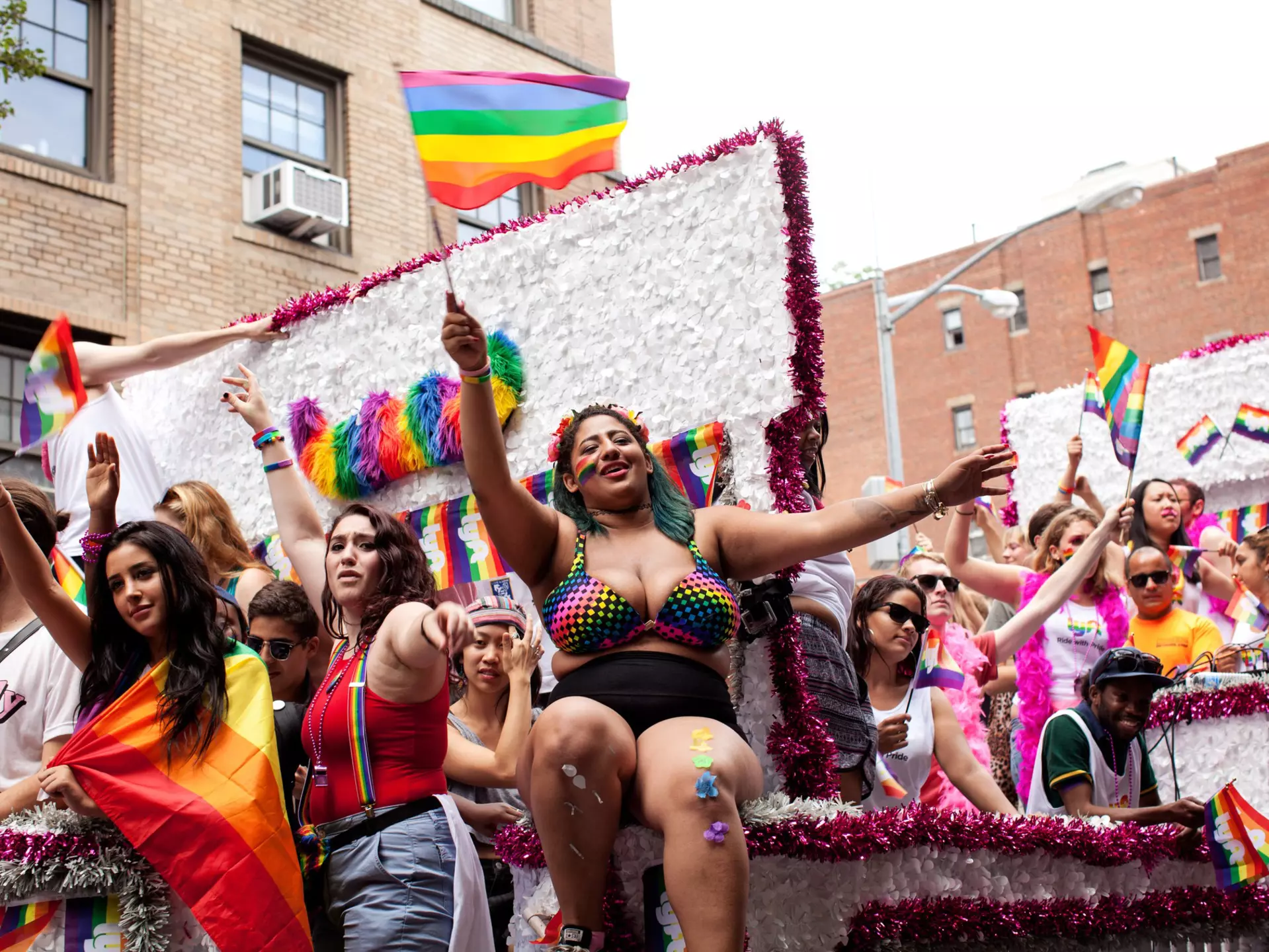 People dressed in bright colors and waving Pride flags on a float in the NYC Pride parade