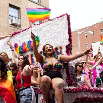 People dressed in bright colors and waving Pride flags on a float in the NYC Pride parade