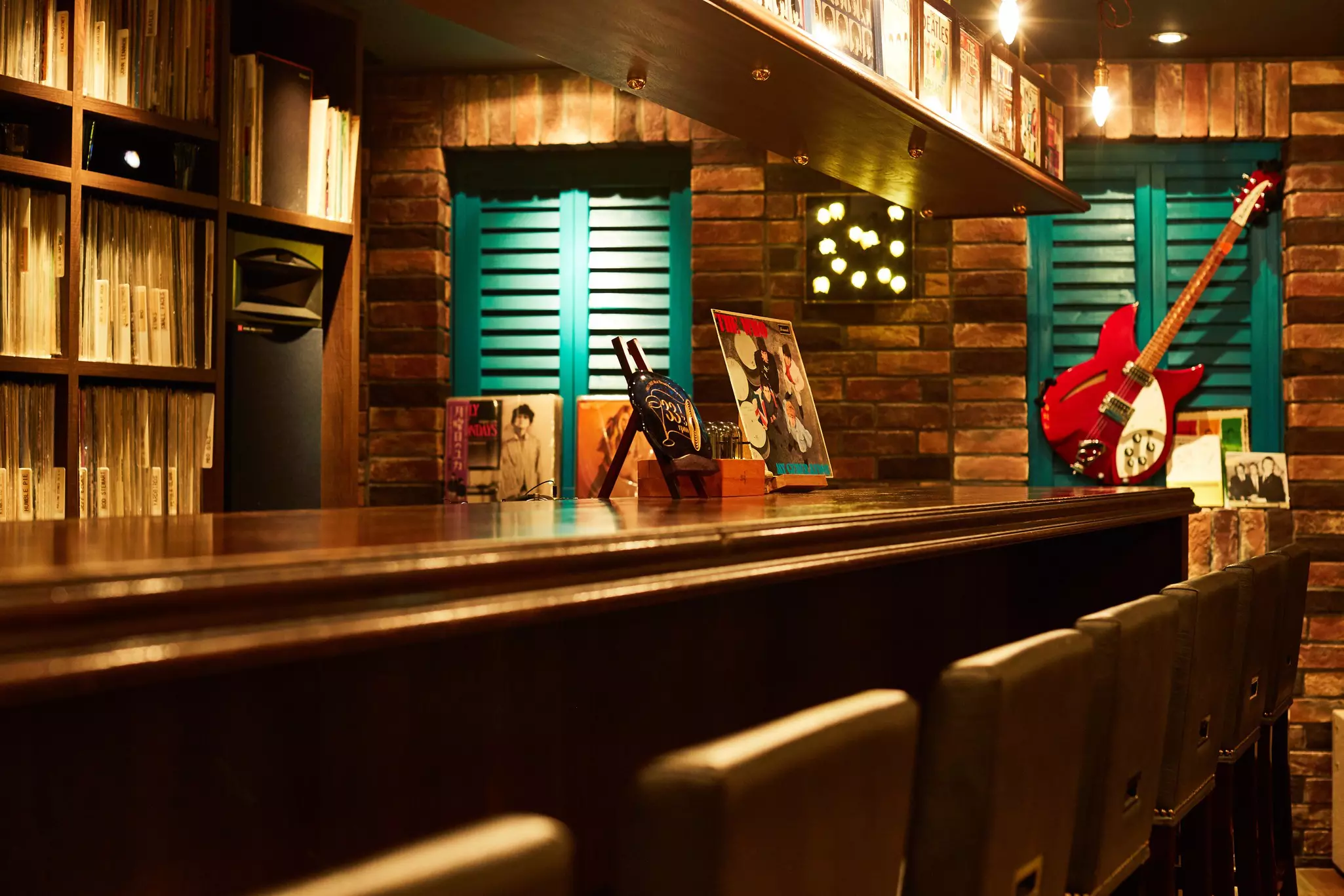 Stools lined up neatly at a bar with a guitar mounted on the wall and album covers decorating the walls.