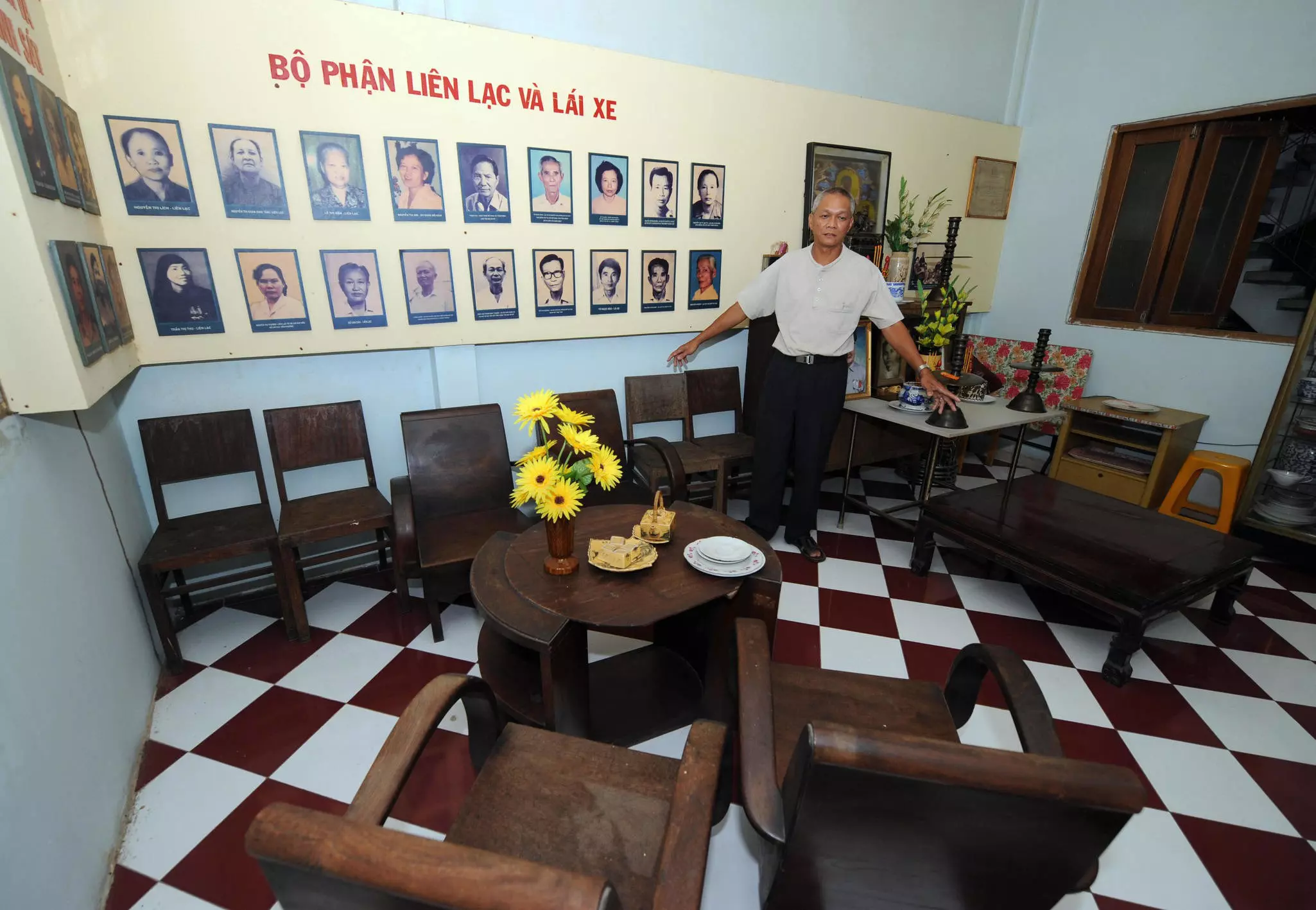 A man and son start a fire as the sun begins to set in the woods of coniferous trees. A small blue tent is near the campsite. They both wear peaked hates and checked shirts.