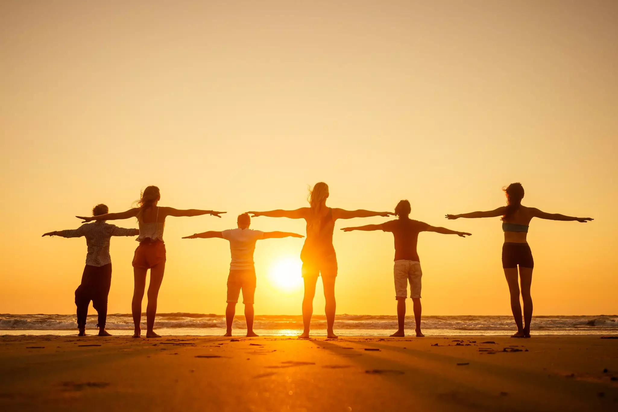 People practicing yoga at dawn on a beach in Goa, India.