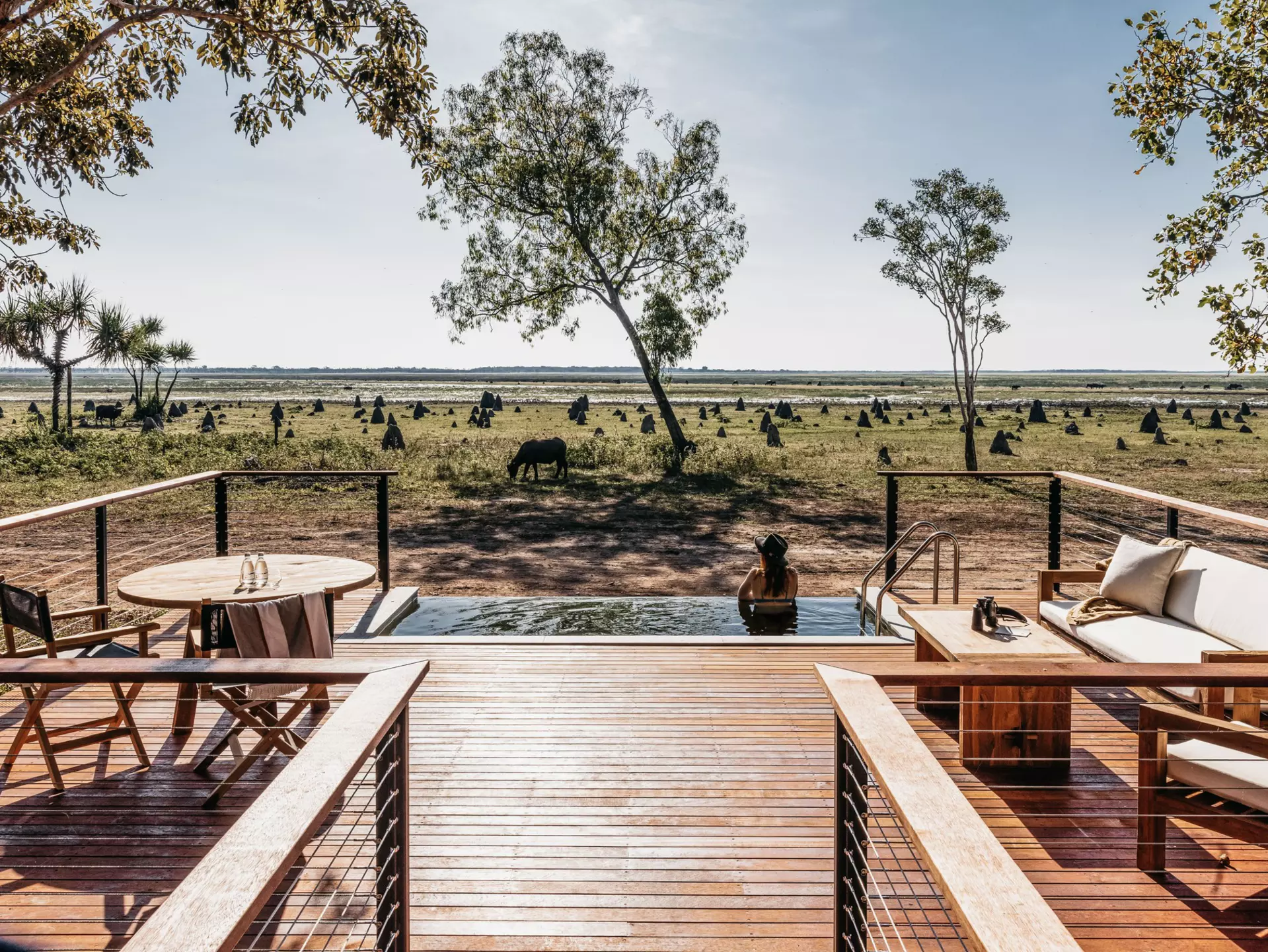 A wooden deck leads to a pool with a woman looking out at the landscape.