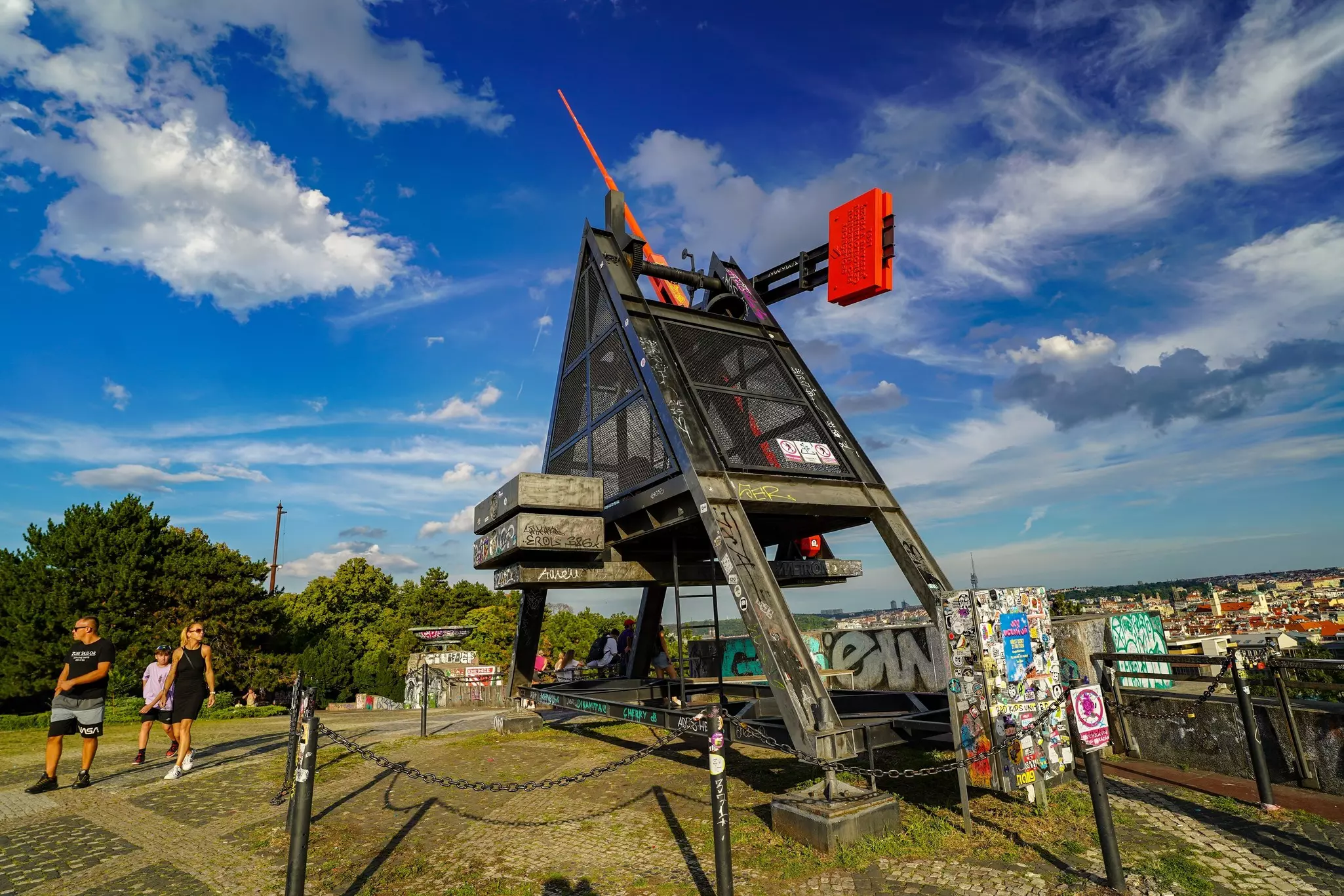A giant metal triangle metronome with a red pointer rising from the grass